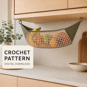 Puede incluir: Una hamaca de frutas de ganchillo color verde oliva colgada bajo un armario de madera, llena de varias frutas incluyendo plátanos, naranjas y manzanas. Un cuadrado blanco muestra el texto CROCHET PATTERN DIGITAL DOWNLOAD.