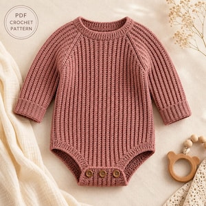 May include: A dusty rose long-sleeve crochet romper featuring a vertical ribbed texture, a round neckline, and three small brown buttons at the bottom closure. The image includes a circular stamp with the text PDF CROCHET PATTERN.