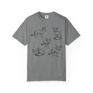 Grey graphic t-shirt featuring a vintage engraved style illustration of multiple fennec foxes arranged in different poses. The foxes are shown sitting, walking, and curled up, with detailed linework creating a naturalist wildlife illustration and desert animal aesthetic.
