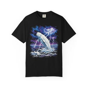 Black Comfort Colors garment-dyed t-shirt featuring a full-color 90s airbrush-style illustration of a white beluga whale breaching from a dark storm ocean beneath forking white lightning bolts and deep cobalt and purple storm clouds — unisex graphic tee.
