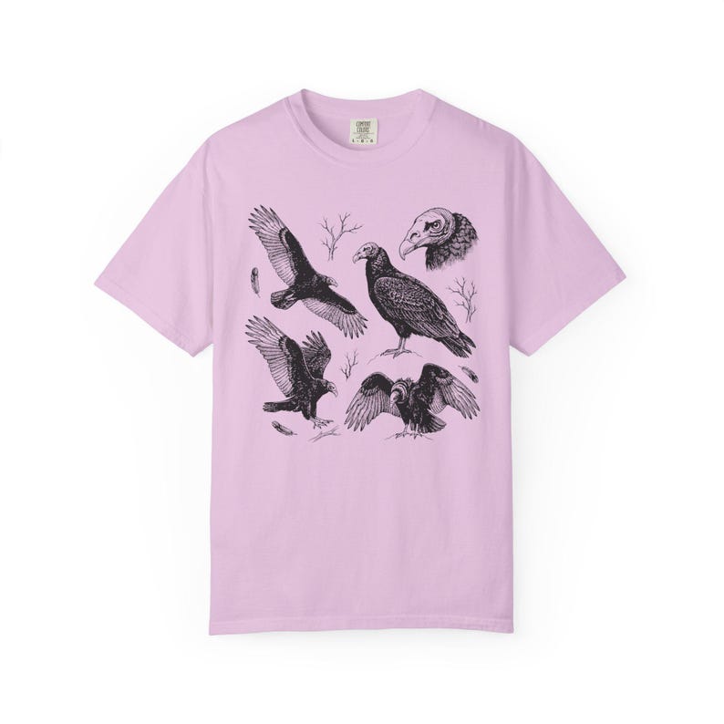 Orchid purple Comfort Colors t-shirt with a vintage engraved illustration of five vultures including one soaring with wings outstretched, one standing with wings half-spread, a close-up portrait showing bare head and hooked beak, one landing with wings fanned, and one spreading wings low in a dominance display, surrounded by bare winter branches and scattered feathers in an antique wildlife field guide etching style.