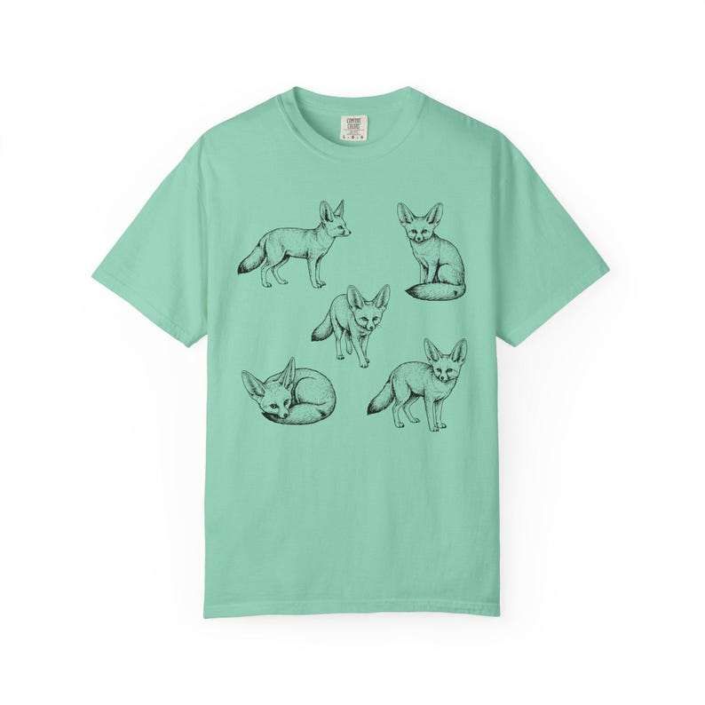 Island reef green graphic t-shirt featuring a vintage engraved style illustration of multiple fennec foxes arranged in different poses. The foxes are shown sitting, walking, and curled up, with detailed linework creating a naturalist wildlife illustration and desert animal aesthetic.