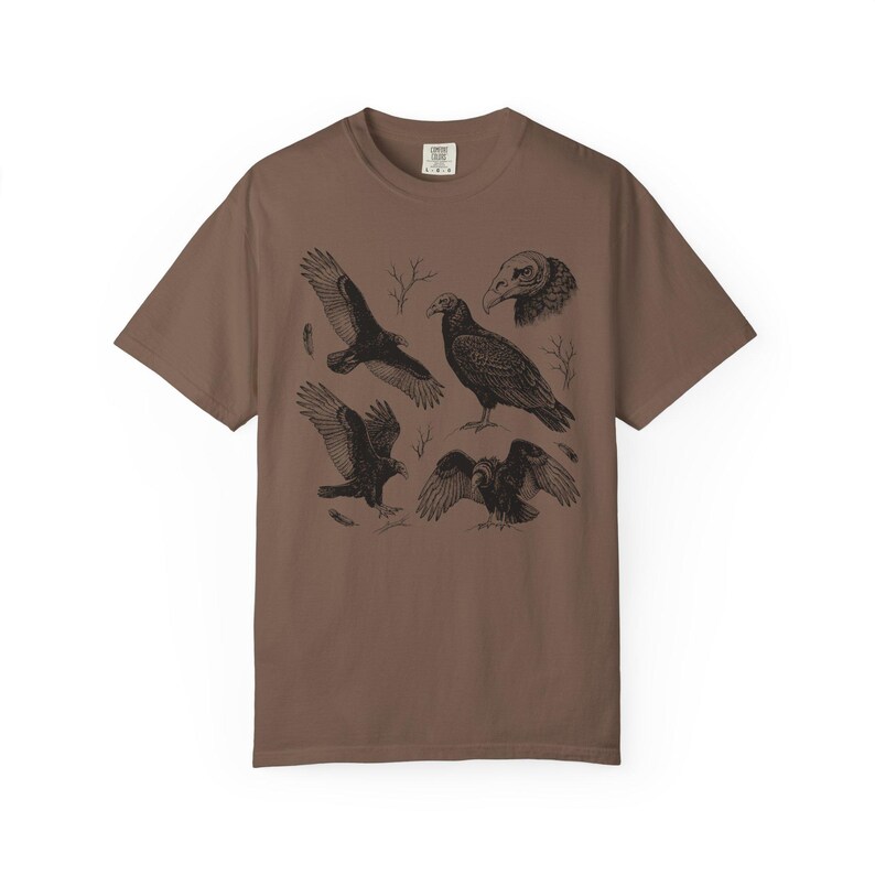 Espresso brown Comfort Colors t-shirt with a vintage engraved illustration of five vultures including one soaring with wings outstretched, one standing with wings half-spread, a close-up portrait showing bare head and hooked beak, one landing with wings fanned, and one spreading wings low in a dominance display, surrounded by bare winter branches and scattered feathers in an antique wildlife field guide etching style.