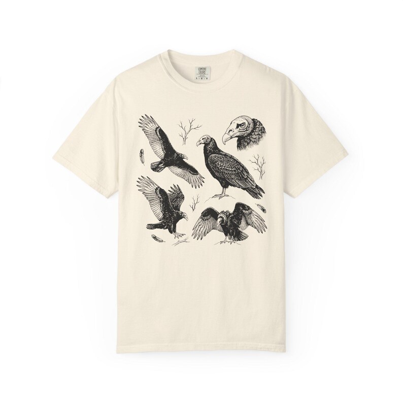 Ivory Comfort Colors t-shirt with a vintage engraved illustration of five vultures including one soaring with wings outstretched, one standing with wings half-spread, a close-up portrait showing bare head and hooked beak, one landing with wings fanned, and one spreading wings low in a dominance display, surrounded by bare winter branches and scattered feathers in an antique wildlife field guide etching style.