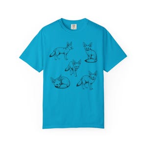 Sapphire blue graphic t-shirt featuring a vintage engraved style illustration of multiple fennec foxes arranged in different poses. The foxes are shown sitting, walking, and curled up, with detailed linework creating a naturalist wildlife illustration and desert animal aesthetic.