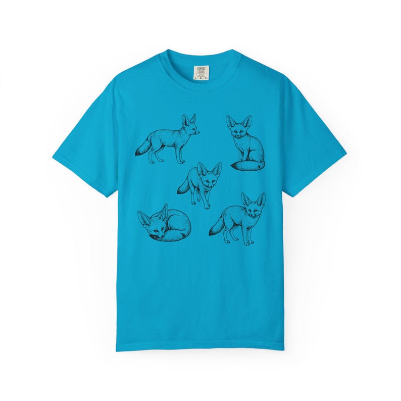 Sapphire blue graphic t-shirt featuring a vintage engraved style illustration of multiple fennec foxes arranged in different poses. The foxes are shown sitting, walking, and curled up, with detailed linework creating a naturalist wildlife illustration and desert animal aesthetic.
