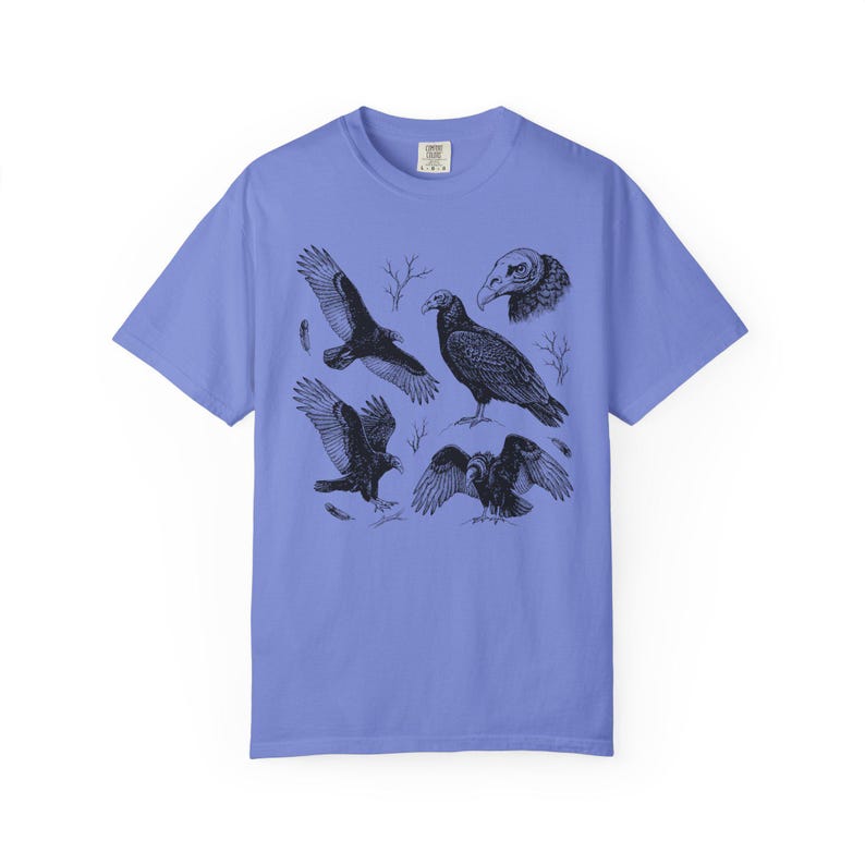Flo blue Comfort Colors t-shirt with a vintage engraved illustration of five vultures including one soaring with wings outstretched, one standing with wings half-spread, a close-up portrait showing bare head and hooked beak, one landing with wings fanned, and one spreading wings low in a dominance display, surrounded by bare winter branches and scattered feathers in an antique wildlife field guide etching style.