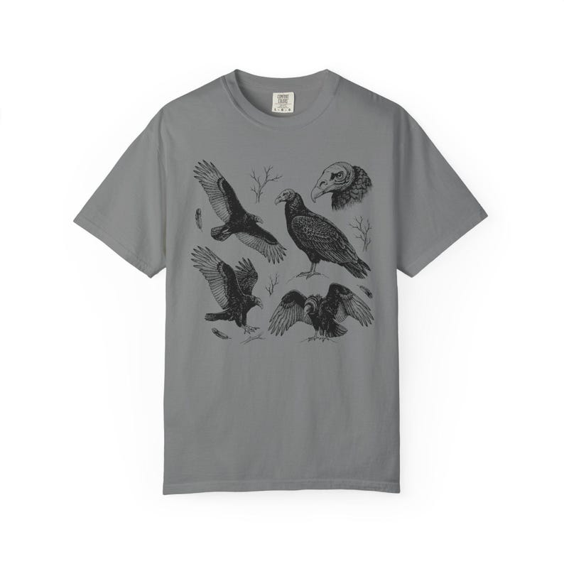 Grey Comfort Colors t-shirt with a vintage engraved illustration of five vultures including one soaring with wings outstretched, one standing with wings half-spread, a close-up portrait showing bare head and hooked beak, one landing with wings fanned, and one spreading wings low in a dominance display, surrounded by bare winter branches and scattered feathers in an antique wildlife field guide etching style.