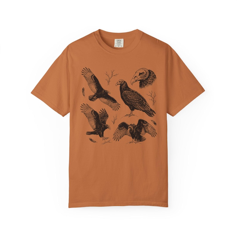 Yam orange Comfort Colors t-shirt with a vintage engraved illustration of five vultures including one soaring with wings outstretched, one standing with wings half-spread, a close-up portrait showing bare head and hooked beak, one landing with wings fanned, and one spreading wings low in a dominance display, surrounded by bare winter branches and scattered feathers in an antique wildlife field guide etching style.