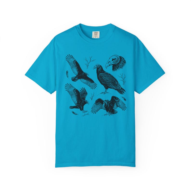 Sapphire blue Comfort Colors t-shirt with a vintage engraved illustration of five vultures including one soaring with wings outstretched, one standing with wings half-spread, a close-up portrait showing bare head and hooked beak, one landing with wings fanned, and one spreading wings low in a dominance display, surrounded by bare winter branches and scattered feathers in an antique wildlife field guide etching style.