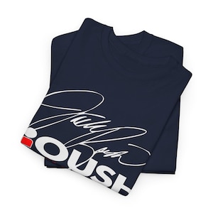 Puede incluir: Dos camisetas azul marino dobladas, con la superior mostrando texto blanco en cursiva y la palabra "PUSH" en letras gruesas. Un acento rojo es visible en la camiseta superior. Las camisetas están hechas de un material suave.