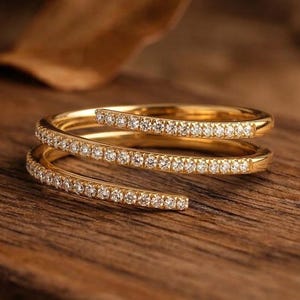 May include: A gold-colored ring with a spiral design, encrusted with small, clear gemstones. The ring is set against a wooden surface, showcasing its intricate details and sparkling stones. The ring's design wraps around the finger.