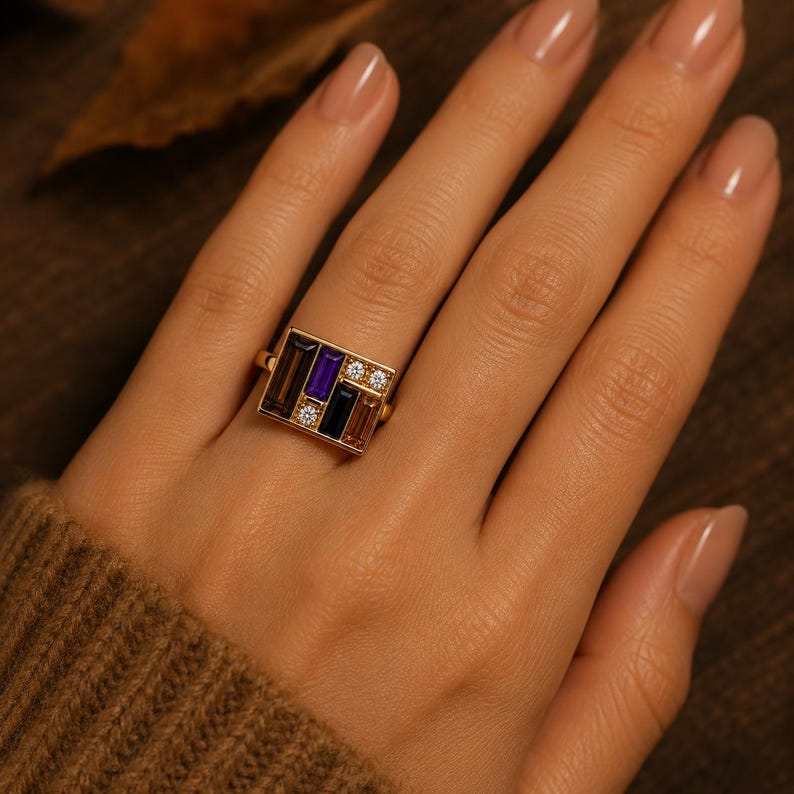 Puede incluir: Un anillo de oro con un dise&ntilde;o rectangular con piedras preciosas de varios colores. El dise&ntilde;o incluye piedras de corte rectangular en tonos marr&oacute;n, morado y negro, acentuadas con peque&ntilde;as piedras redondas y claras. El anillo est&aacute; engarzado en una banda de oro.