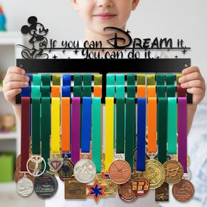 May include: Black metal medal display with colorful ribbons, featuring a Mickey Mouse silhouette and the text "If you can dream it, you can do it." The display holds various medals with different designs.