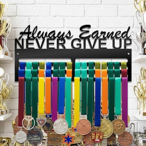 May include: Black metal medal display rack with the words "Always Earned NEVER GIVE UP" in a decorative font. The rack holds colorful ribbons with medals attached. Trophies are visible on shelves in the background.