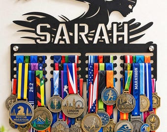 May include: A black metal wall-mounted medal display rack featuring a silhouette of a swimmer at the top and the name SARAH in cut-out letters. The rack holds numerous colourful ribbons with various marathon and race finisher medals.
