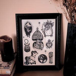 May include: Black framed art print with various black and white illustrations. The illustrations include a Furby smoking, a heart with a banner, a pony, and an 8-ball.