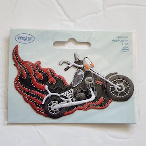 May include: Embroidered motorcycle patch with flames. The patch features a black motorcycle with white and orange accents, set against a backdrop of red and black flames. The patch is on a light blue backing.