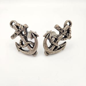 May include: A pair of silver-toned anchor stud earrings. Each earring features a detailed anchor design with rope detailing. The earrings are set against a white background, highlighting the nautical theme.