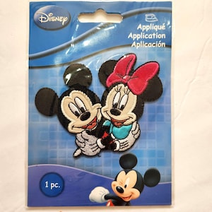 May include: A Disney brand iron-on embroidered patch featuring Mickey and Minnie Mouse. The patch shows Mickey and Minnie embracing, with Minnie wearing a bright pink bow. The packaging includes the text Appliqué Application Aplicación and 1 pc.