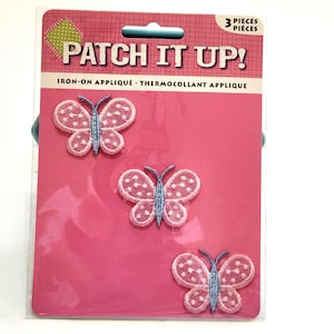 May include: Three embroidered butterfly iron-on appliqués packaged on a pink card labeled PATCH IT UP! Each butterfly features light pink wings with white dot details and a light blue body with two antennae, designed for fabric decoration.