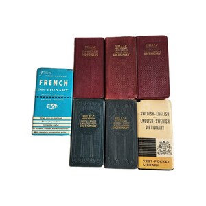 May include: A collection of vintage dictionaries in various colors. The books include a blue French dictionary, several red dictionaries, and green and tan dictionaries. The text on the books includes the words "French", "English", and "Dictionary".