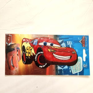 May include: A Disney Pixar Cars Lightning McQueen embroidered applique patch in red, yellow, and black. The patch features the number 95, blue eyes, and a smiling mouth. It is packaged on a blue and orange cardboard backing with the text 1 pc.