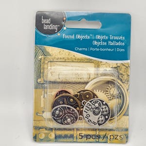 May include: A package of five steampunk-style charms. The charms are in various metallic finishes, including silver, bronze, and copper. The package has the text "Found Objects" and "Charms".
