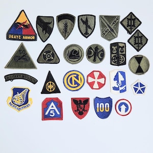 May include: A collection of twenty-six embroidered military patches in various shapes including triangles, circles, shields, and diamonds. The patches feature diverse symbols, colors, and text such as USATC ARMOR, MILITARY INSTITUTE, and PACIFIC AIR FORCES.