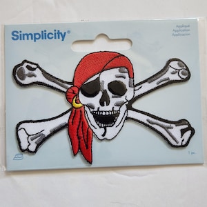 May include: Embroidered pirate skull patch with a red bandana, black eye patch, and crossed bones. The patch is white, black, red, and yellow. The package has the word "Simplicity" printed on it.