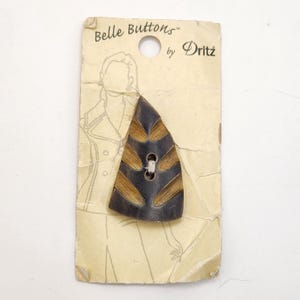 May include: A vintage Belle Buttons by Dritz button on its original packaging. The button is a dark brown, triangular shape with lighter brown, leaf-like accents. The packaging is a light tan color with a drawing of a person.