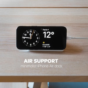Peut inclure: Un dock Air minimaliste pour iPhone affichant l'heure et la température à Paris. L'écran noir affiche un cadran d'horloge et la température est de 12 degrés. Le dock est blanc et connecté à un câble blanc. Le texte "AIR SUPPORT" est visible.