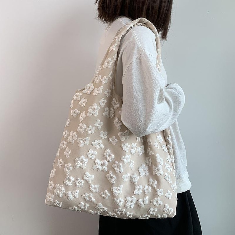Pu&ograve; includere: Una borsa tote beige con ricami floreali bianchi. La borsa ha una tracolla ed &egrave; realizzata in un tessuto morbido e strutturato. Il design floreale &egrave; distribuito uniformemente sulla superficie della borsa, creando un'estetica delicata e femminile.