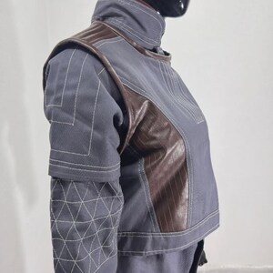 May include: A gray and brown jacket with white stitching details. The jacket features a high collar, brown leather-like panels, and geometric patterns on the sleeves. The design is modern and structured, suitable for cosplay or fashion.