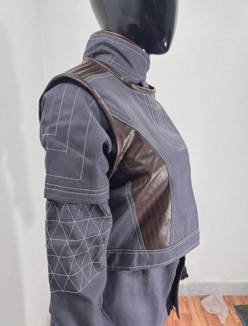 May include: A gray and brown jacket with white stitching details. The jacket features a high collar, brown leather-like panels, and geometric patterns on the sleeves. The design is modern and structured, suitable for cosplay or fashion.