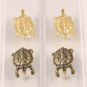 Op de afbeelding: Vier kleine, gedetailleerde schildpadbeeldjes in goud- en bronstinten. Twee zijn goudkleurig, met getextureerde schilden en uitgestrekte poten. De andere twee zijn bronskleurig, met vergelijkbare details. De schildpadden zijn in een rasterpatroon gerangschikt.