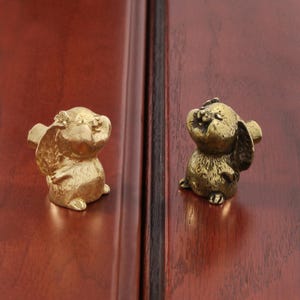 May include: A set of three ceramic mugs with a speckled, matte finish. The mugs are in shades of cream, light gray, and dark gray. Each mug has a simple, minimalist design and a rounded handle.