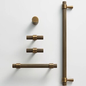 May include: A collection of antique brass cabinet hardware, including a knob, two T-bar pulls, a long bar pull, and a large handle. The hardware features a textured, dotted pattern and is designed for furniture or cabinetry.