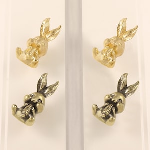 Könnte beinhalten: Vier kleine, goldfarbene Hasenfiguren. Jeder Hase sitzt und hält eine Karotte. Die Hasen haben detaillierte Merkmale, einschließlich langer Ohren und einer strukturierten Oberfläche.