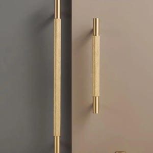 Könnte beinhalten: Goldfarbenes Schrankbeschlags-Set, bestehend aus zwei langen Griffen, zwei kleineren Griffen und zwei Knöpfen. Die Griffe und Knöpfe haben ein strukturiertes, gepunktetes Muster. Das Wort "NURLIN" ist auf einem blauen Rechteck aufgedruckt.