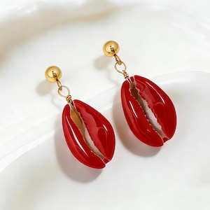 May include: A pair of red shell-shaped earrings with gold-colored accents. The earrings have a glossy finish and are suspended from small gold-colored ball studs. The shells are approximately 1.5 inches long.