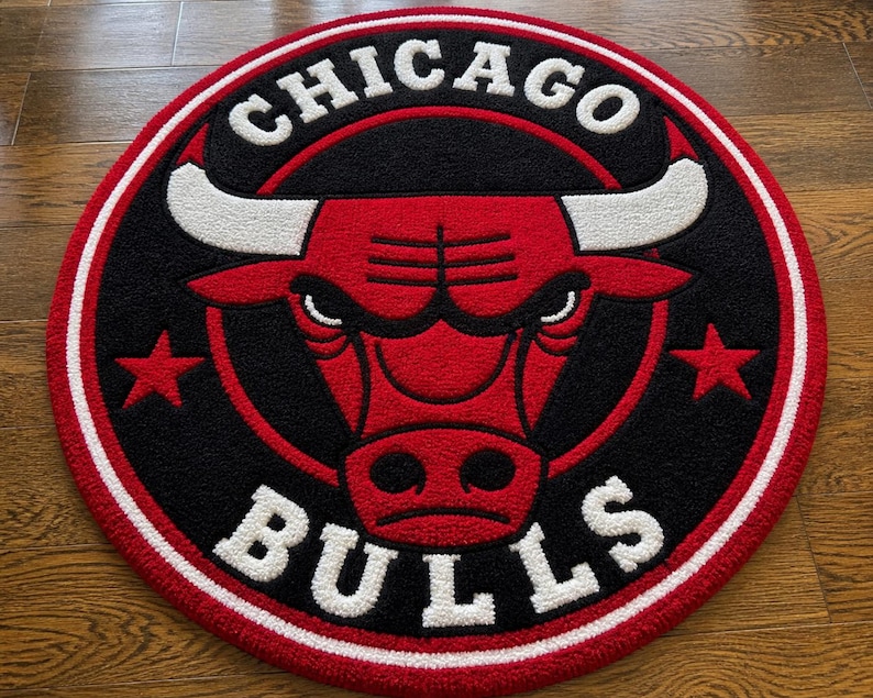 May include: A round rug featuring the Chicago Bulls logo. The rug has a red bull head in the center, surrounded by a black background. The words "CHICAGO" and "BULLS" are in white, with red stars on either side of the bull's head. The rug is trimmed with a white and red border.