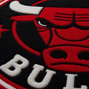 May include: Circular rug featuring the Chicago Bulls logo. The design includes a red bull head, a red star, and the word "BULLS" in white. The background is black with a red border.