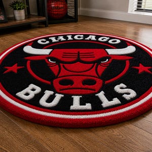 May include: A round rug featuring the Chicago Bulls logo. The rug has a black center with a red bull head and white lettering. A red and white border surrounds the logo. The rug is on a wooden floor.