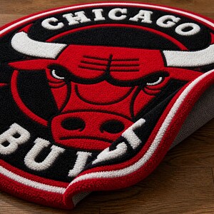 May include: A round rug featuring the Chicago Bulls logo. The rug has a red, black, and white color scheme. The logo includes a red bull head with white horns, the words "CHICAGO" and "BULLS" in white.