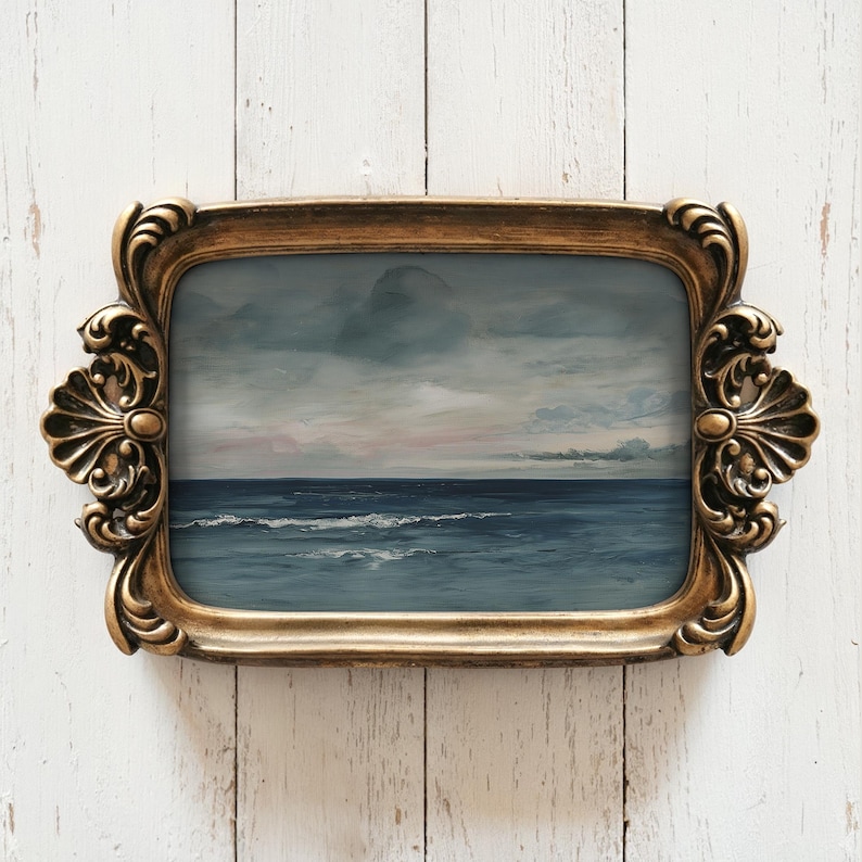May include: A rectangular, gold-colored decorative tray with ornate scrollwork and handles. The tray holds a painting of a seascape with a dark blue ocean, white waves, and a cloudy sky with hints of pink.