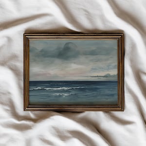May include: A framed seascape painting depicts a moody ocean scene. The artwork features a dark blue sea with white-capped waves under a cloudy sky with hints of pink and gray. The frame is a warm, golden brown.