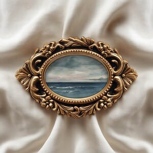 May include: An oval-shaped, antique gold-colored frame with an ocean landscape painting. The frame has ornate floral and scrollwork details. The painting depicts a seascape with a cloudy sky and blue water. The frame is set against a white, textured fabric.