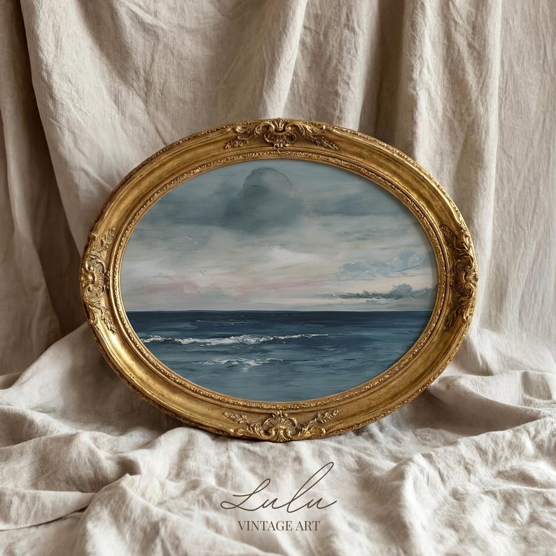 May include: An oval-shaped vintage art piece featuring a seascape painting. The artwork is framed in a gold, ornate frame. The painting depicts a blue ocean under a cloudy sky with hints of pink. The text "Lulu Vintage Art" is at the bottom.