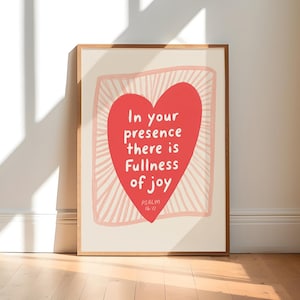 Puede incluir: Una lámina enmarcada con un gran corazón rojo centrado sobre un fondo crema. Dentro del corazón, el texto en blanco dice: In your presence there is Fullness of joy, con el texto Psalm 16:11 debajo. Un borde rosa con rayos de sol rodea el corazón.